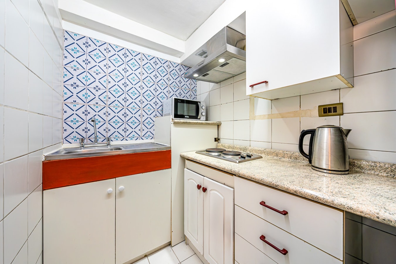 Cocina con azulejo decorativo, lavaplatos, cocina, microondas y hervidor