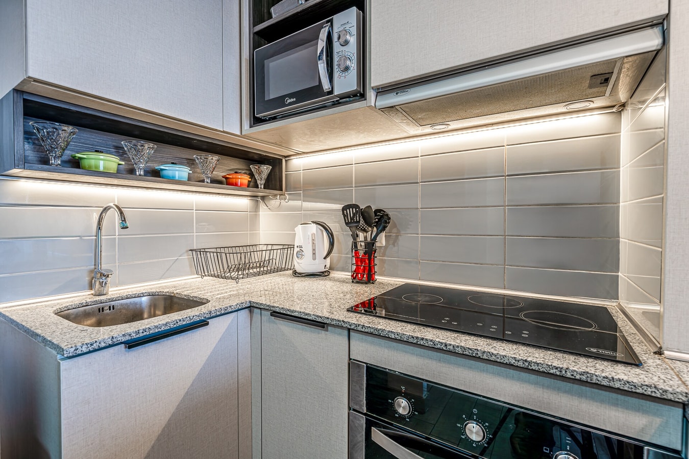 Detalle de la cocina con encimera eléctrica, campana extractora, horno y utensilios sobre el mesón