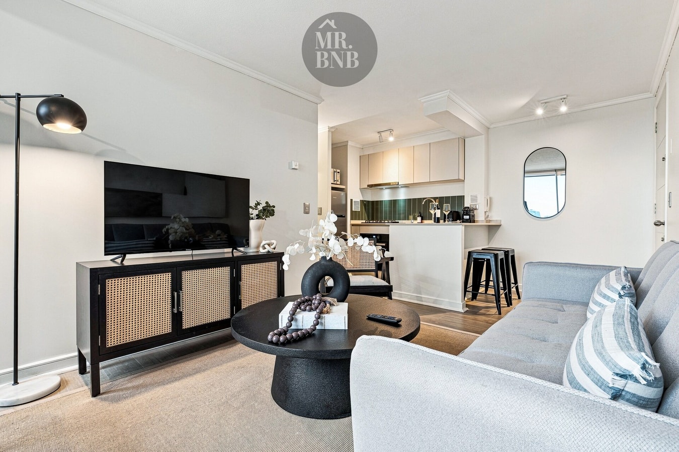 Living con sofá, mueble de TV, mesa de centro y cocina con barra y taburetes al fondo