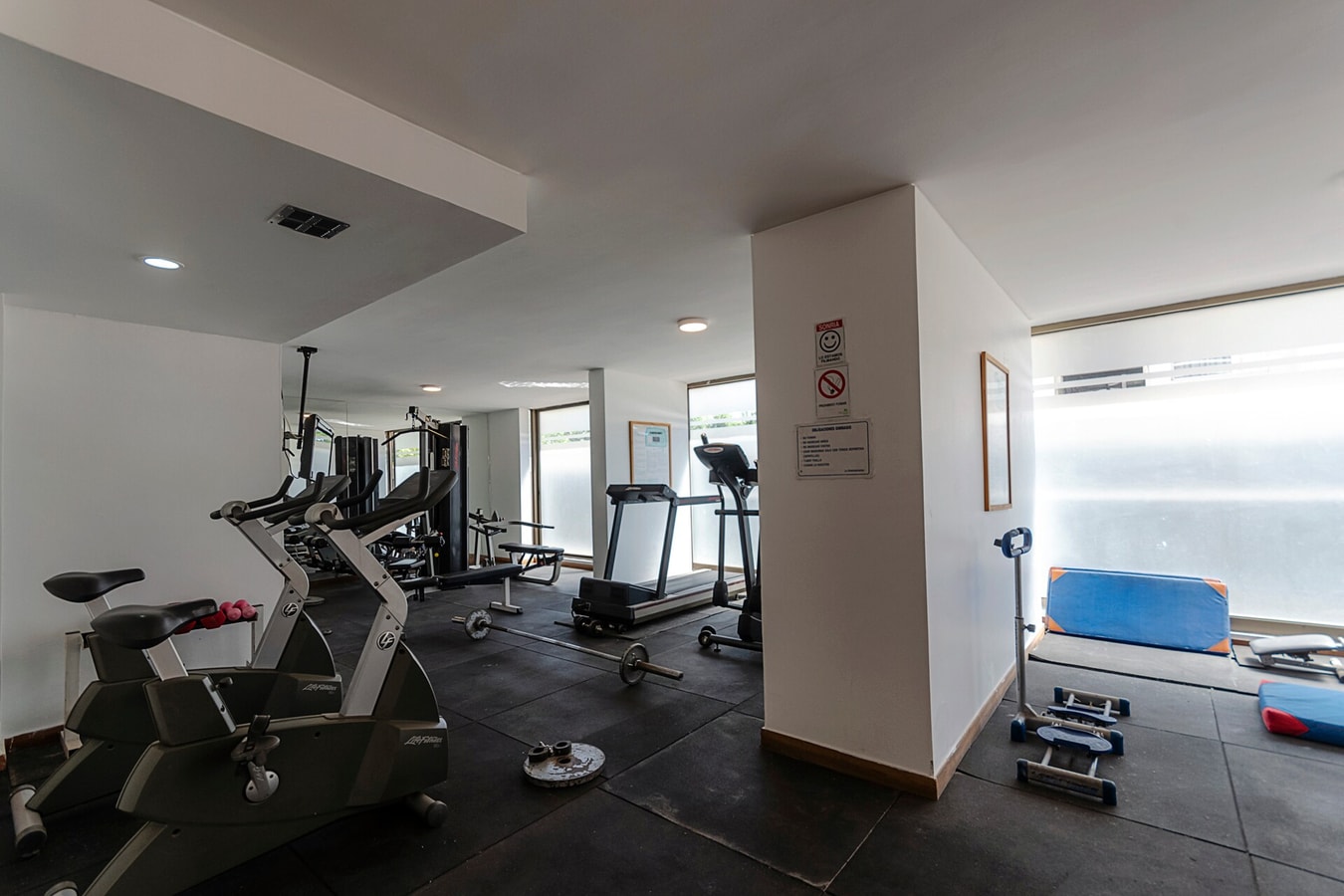 Gimnasio del edificio con máquinas, trotadora, bicicleta estática y colchoneta