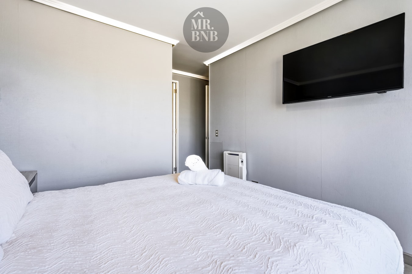 Dormitorio con cama, TV en la pared, ventanal con cortina y calefactor