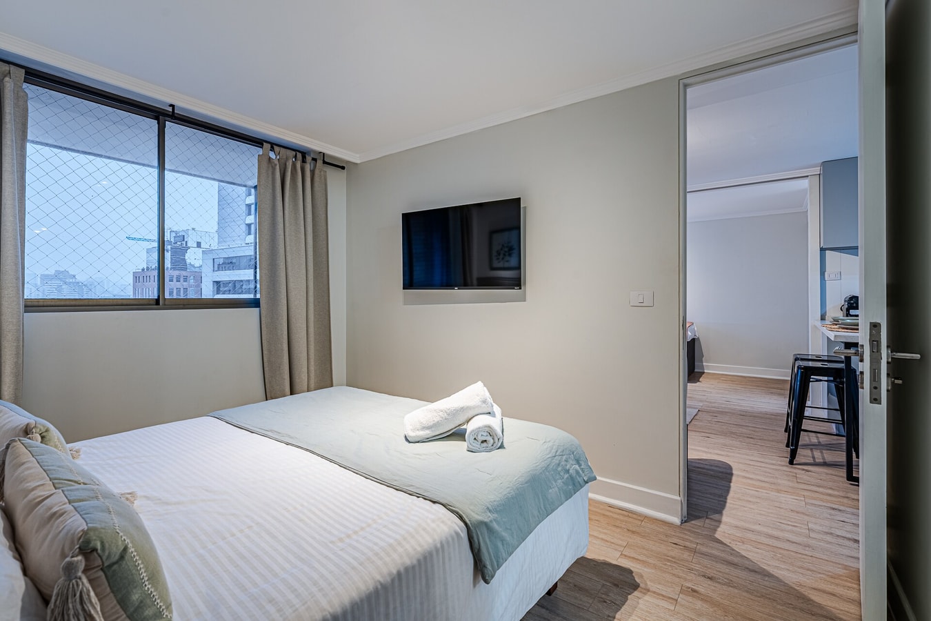 Dormitorio con cama, TV montada y ventanal con vista a la ciudad