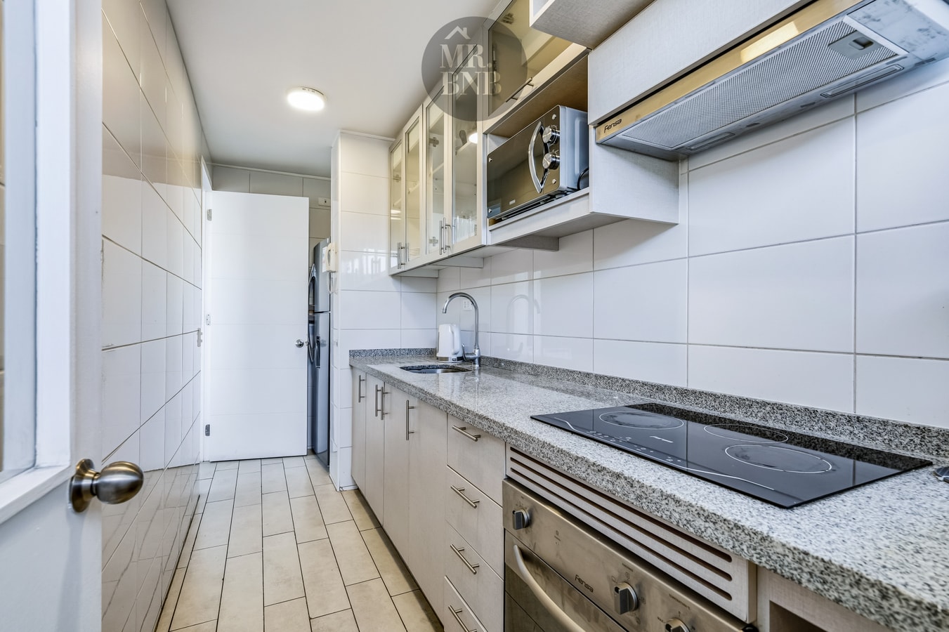 Cocina con encimera de granito, campana, microondas empotrado y refrigerador