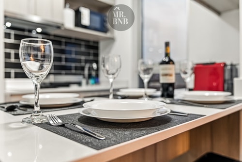 Mesa puesta con plato, copas y una botella de vino sobre la encimera de cocina.