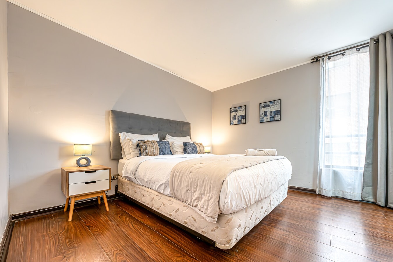 Dormitorio con cabecera tapizada gris, cama con ropa de cama clara y cortinas