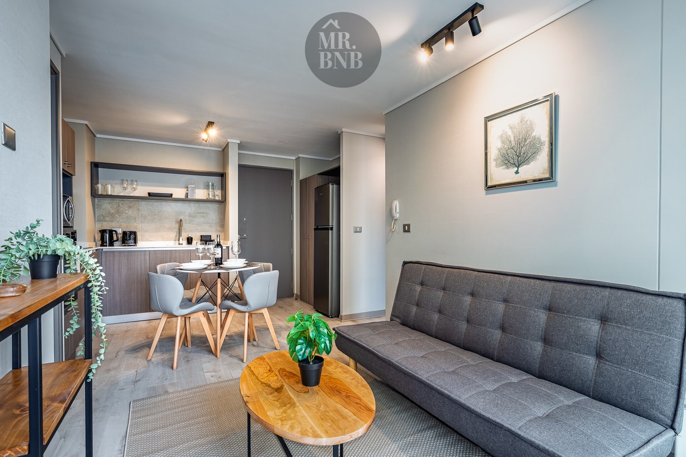 Living con sofá gris, mesa de centro y pequeño comedor junto a la cocina.