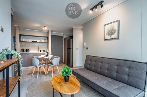 Living con sofá gris, mesa de centro y pequeño comedor junto a la cocina.