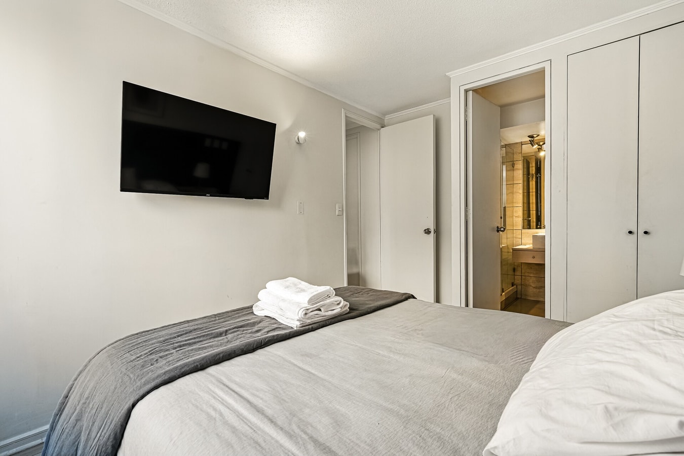 Dormitorio con cama, televisor en la pared y closet con puertas blancas