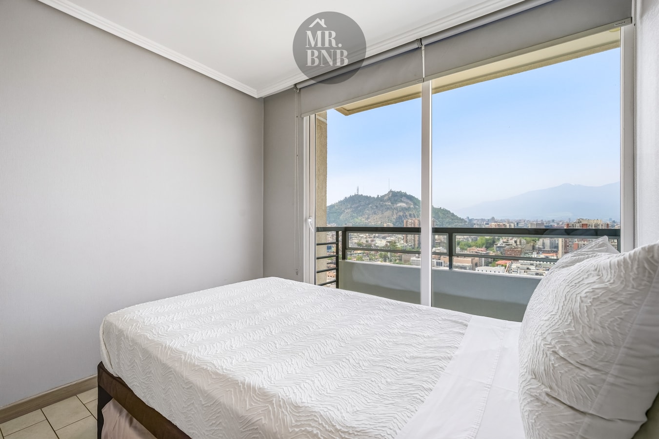 Dormitorio con cama matrimonial y ventanal con vista a la ciudad y cerros