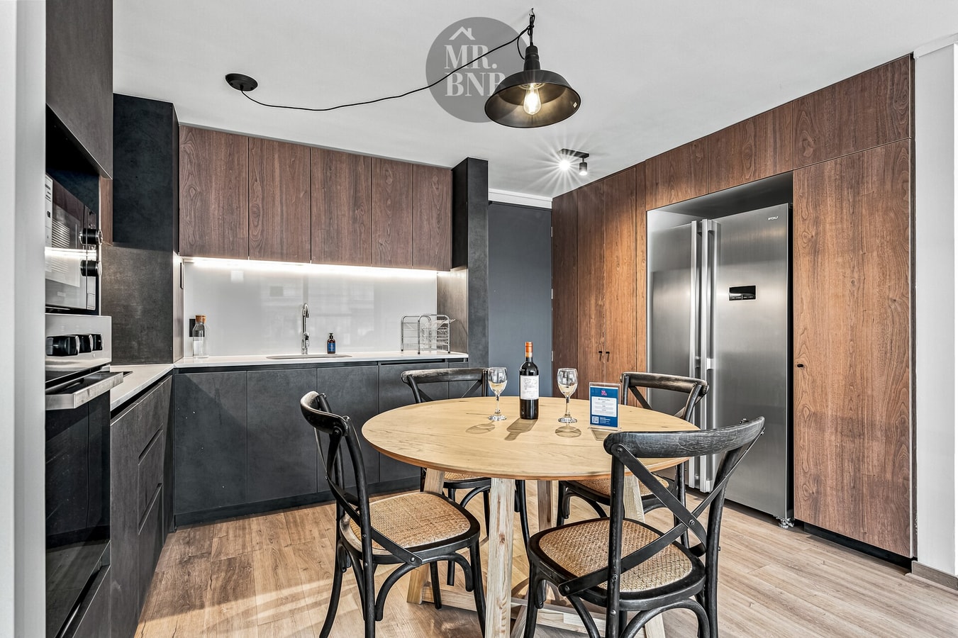Cocina integrada al comedor, con muebles oscuros, mesa redonda de madera y sillas.