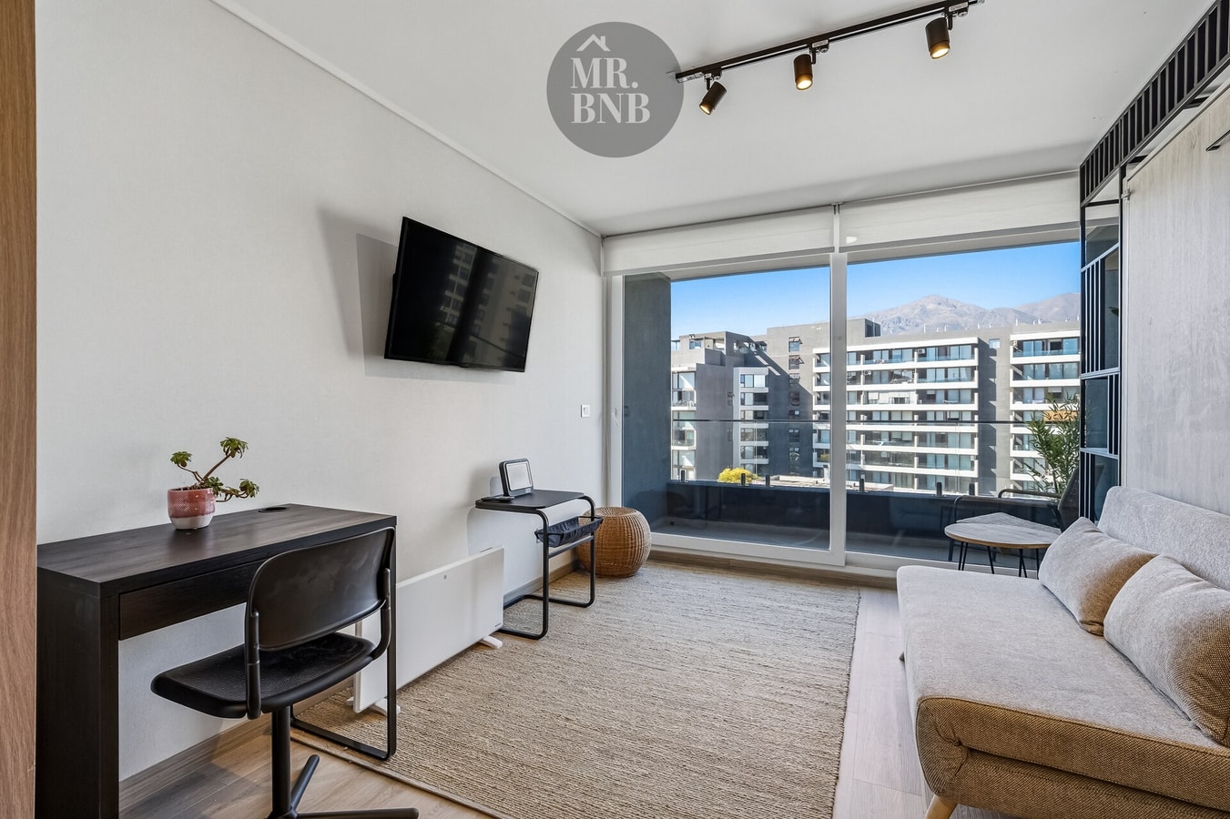 Estudio con escritorio, silla, TV montada y ventanal con vista a la cordillera