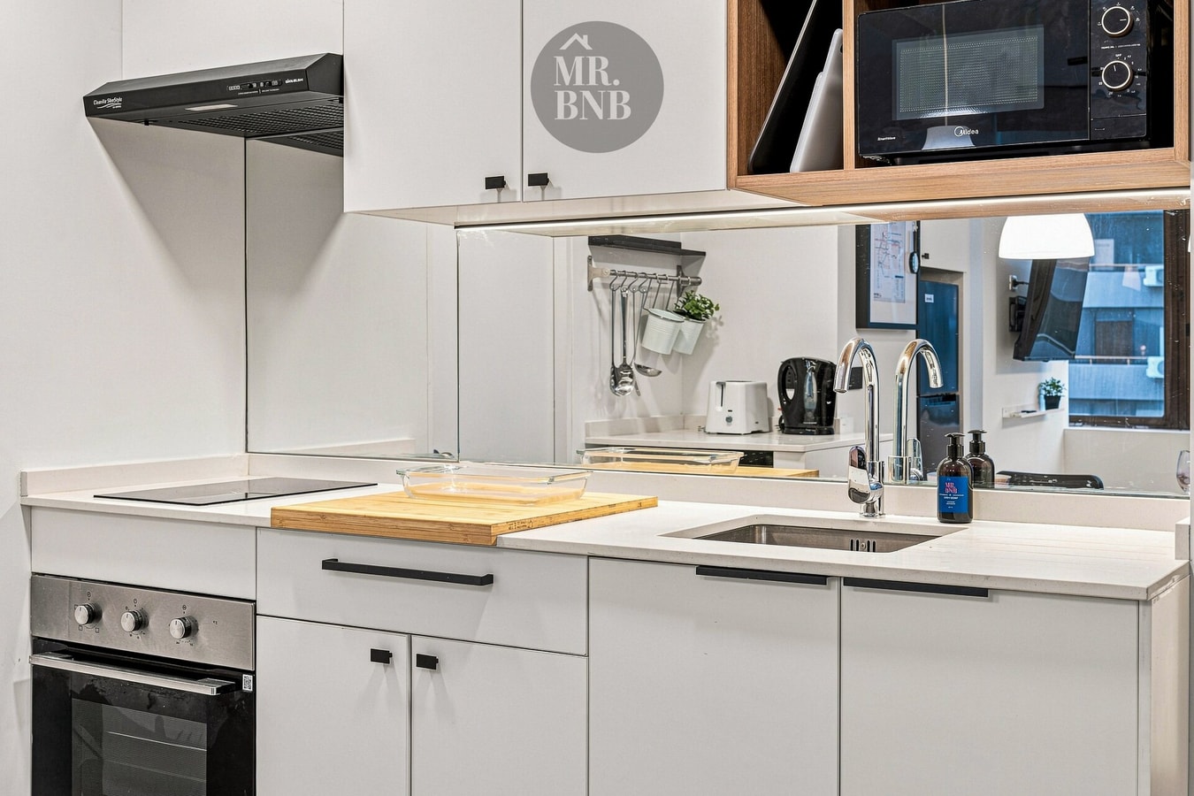 Cocina blanca con encimera eléctrica, horno, microondas y grifería.