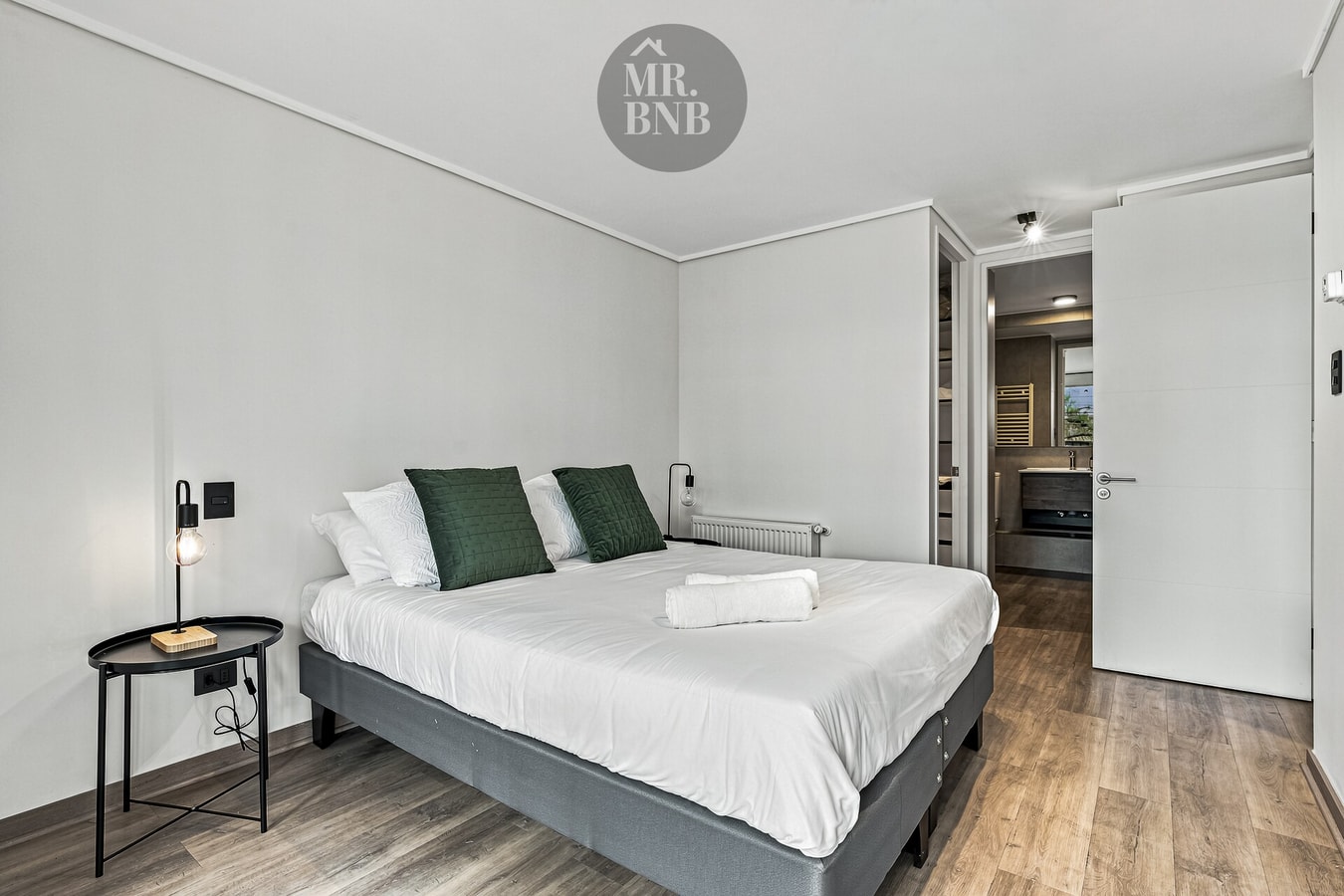 Dormitorio con cama de dos plazas, cojines verdes, veladores y puerta hacia el clóset.
