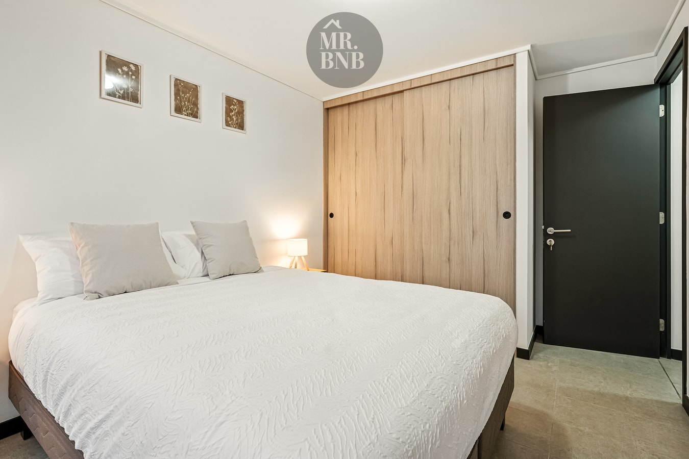 Dormitorio con cama, cuadros decorativos y closet de madera junto a la puerta.