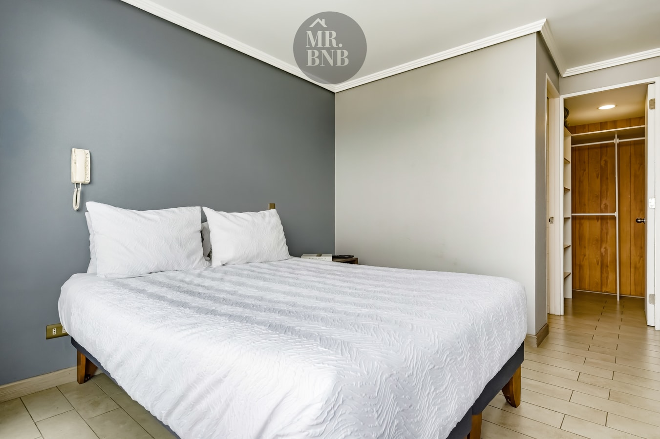 Dormitorio con cama matrimonial, citófono en la pared y clóset de madera al fondo