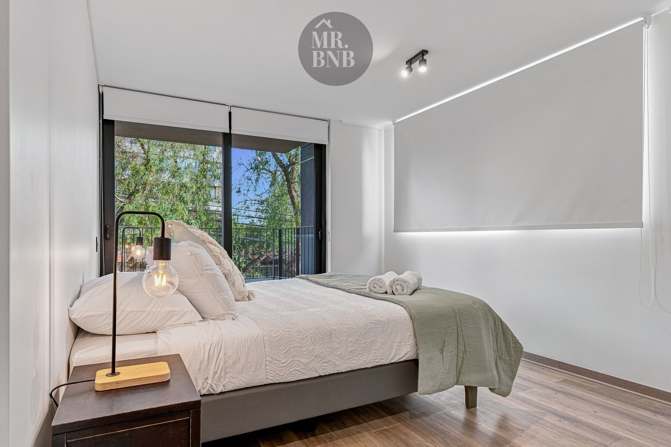 Dormitorio con cama doble, velador y ventanal amplio con cortina