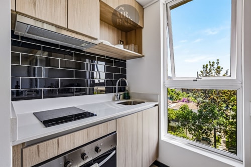 Cocina con encimera eléctrica, horno, campana y ventana con vista al Manquehue