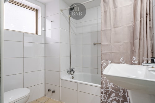 Baño con tina, cortina floral, lavamanos y ventana