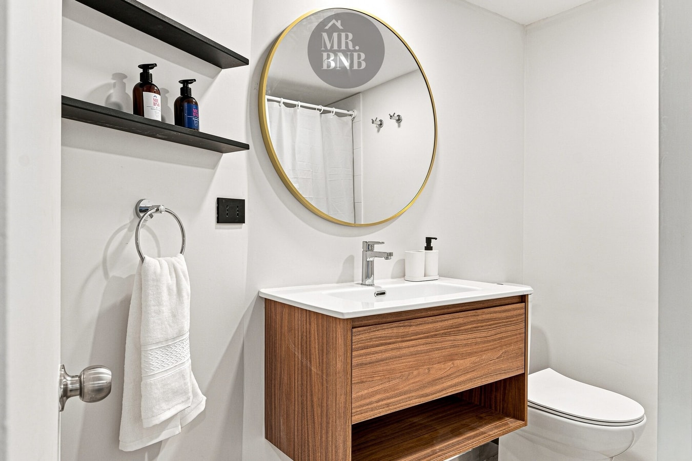 Baño con lavamanos de madera, espejo redondo y amenities en repisa.