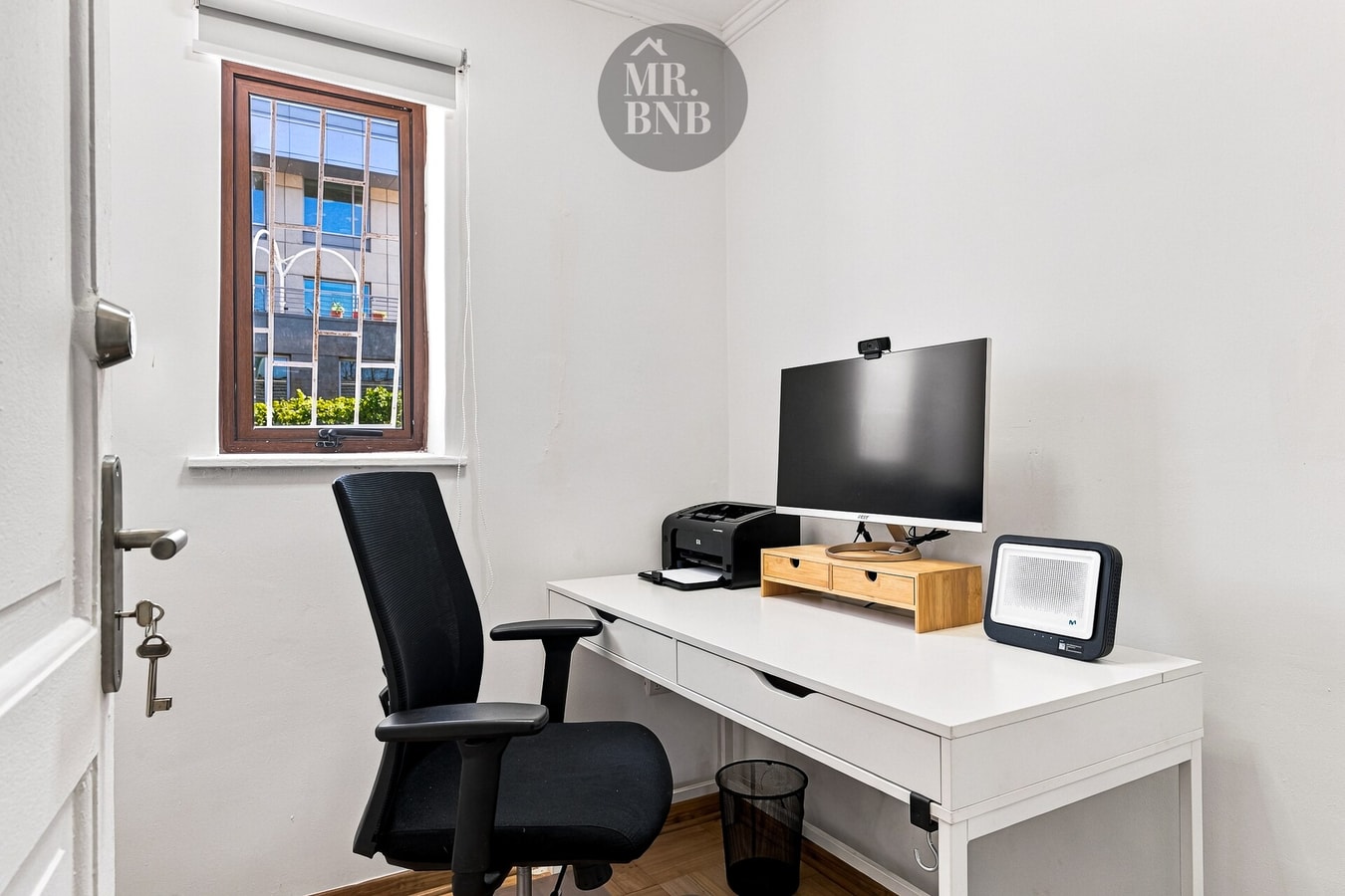 Pieza de trabajo con monitor grande, impresora y silla de escritorio.