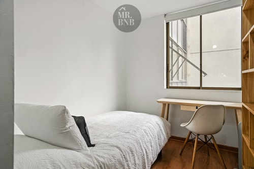 Dormitorio con cama individual, escritorio y silla junto a la ventana