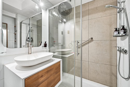 Baño con lavamanos ovalado sobre mueble de madera, ducha de vidrio y amenities