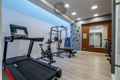 Gimnasio del edificio con trotadora, bicicletas y muro de escalada