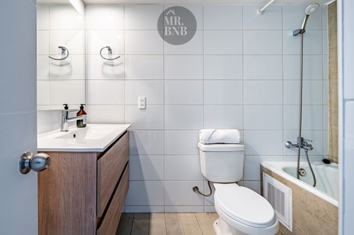 Baño con dos lavamanos, inodoro, tina con ducha y toallas