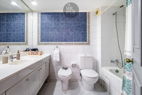 Baño con azulejo azul patronado, tina, bidé, inodoro y lavamanos con doble grifería
