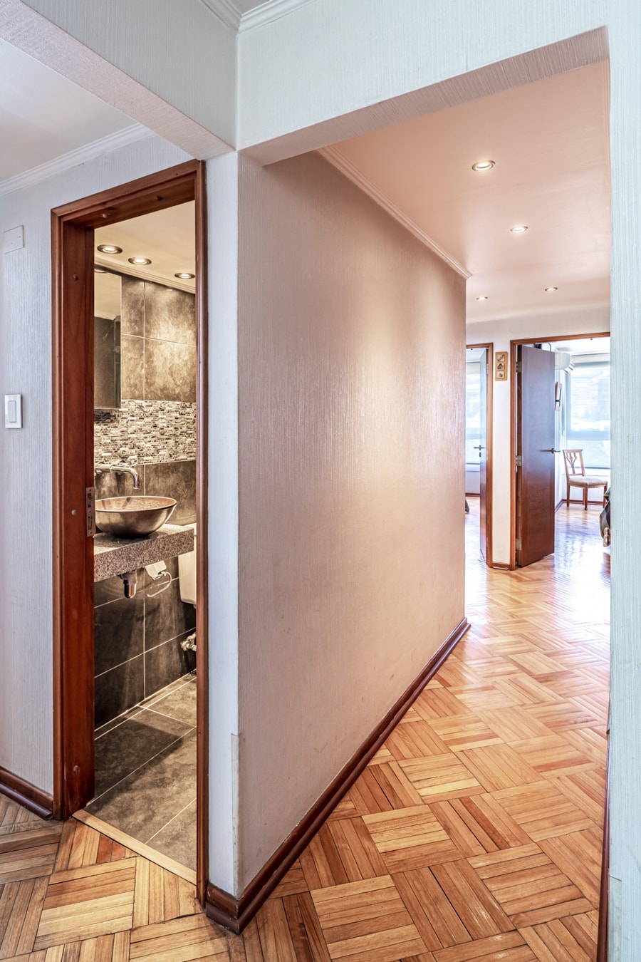 Pasillo interior de parqué que conecta los dormitorios con el living, con puerta abierta hacia un baño.