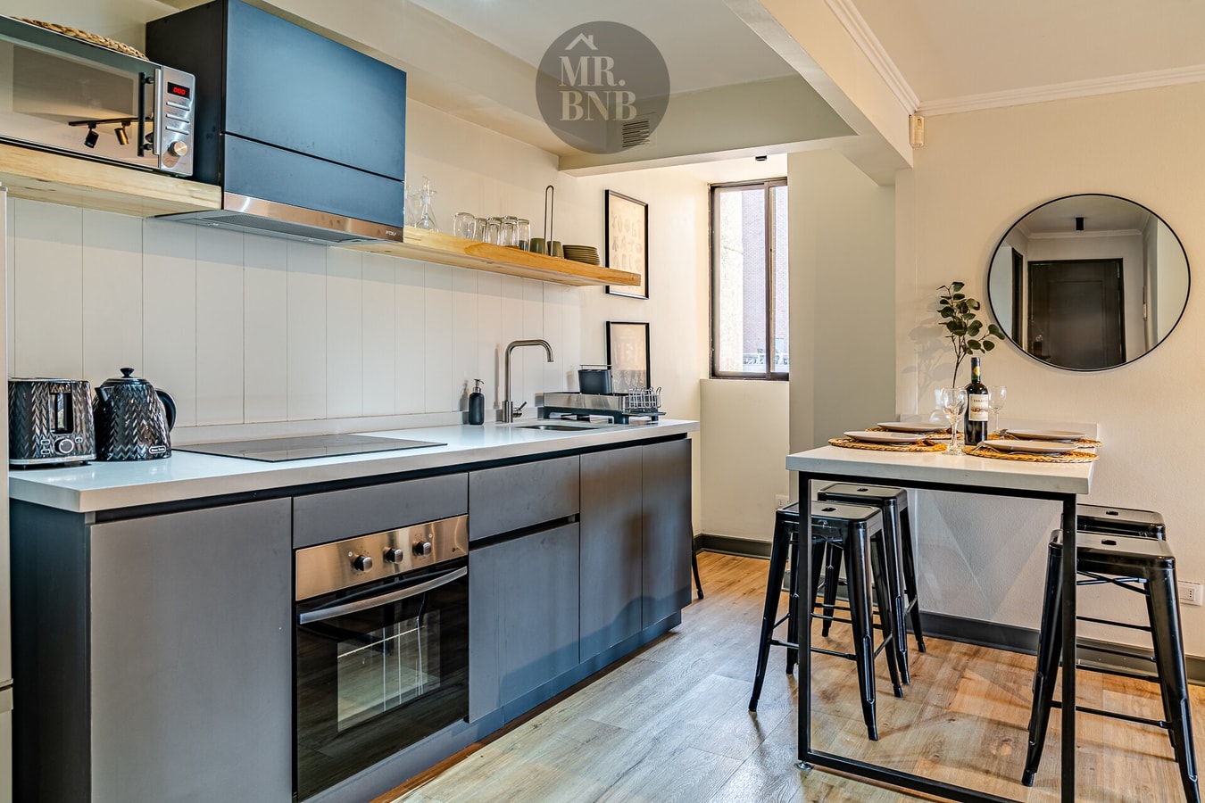 Cocina con muebles bajos oscuros, microondas, horno empotrado y barra alta con dos banquetas