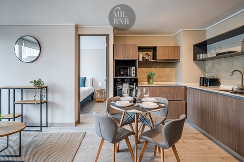 Cocina equipada con muebles de madera, comedor con mesa redonda y vista a dormitorio al fondo.