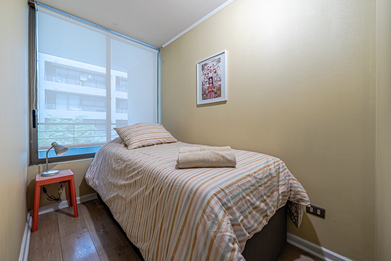 Dormitorio con cama individual, cubrecama a rayas y ventana