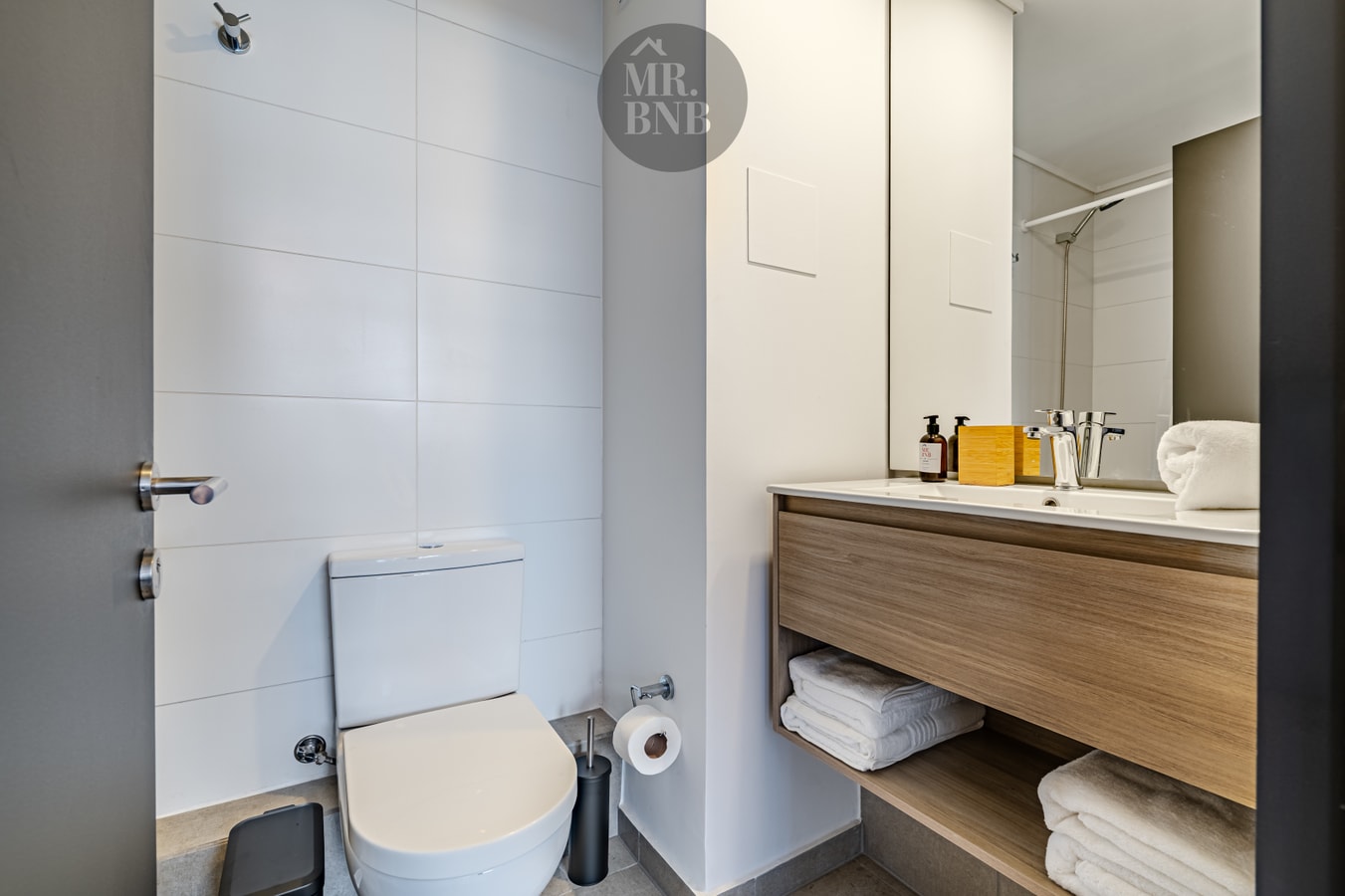 Baño con inodoro, mueble de madera con lavamanos, espejo de cuerpo entero y toallas dobladas en las repisas