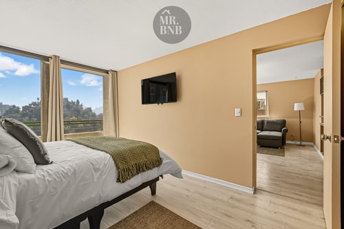 Dormitorio con cama, manta verde y puerta abierta hacia otro ambiente