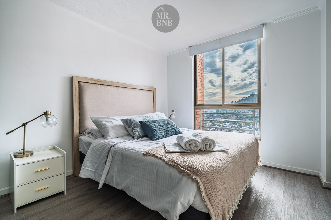 Dormitorio con cama matrimonial, respaldo tapizado y ventanal con vista a la ciudad y los cerros