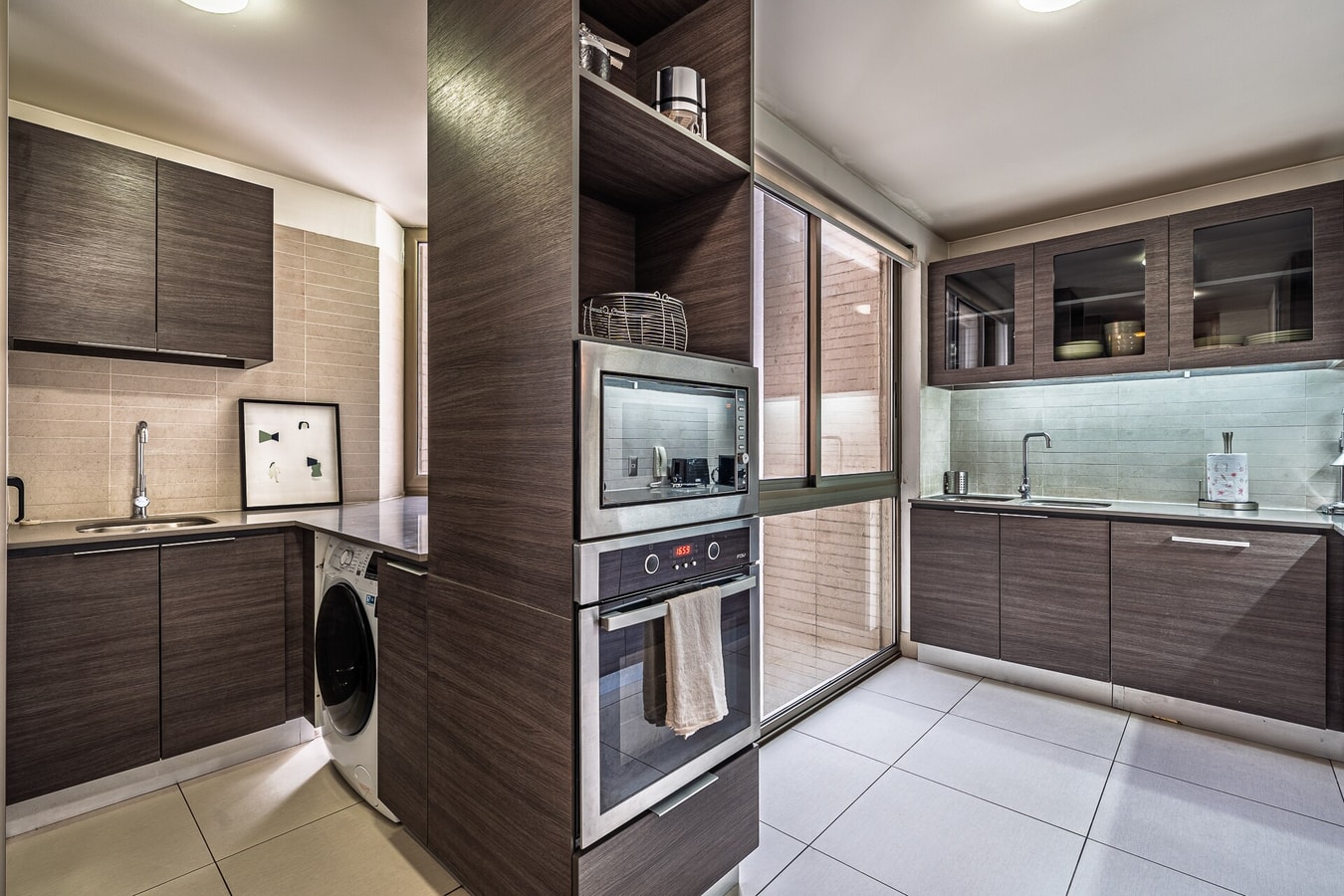 Cocina con muebles oscuros, horno empotrado y lavadora integrada.