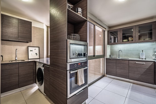 Cocina con muebles oscuros, horno empotrado y lavadora integrada.
