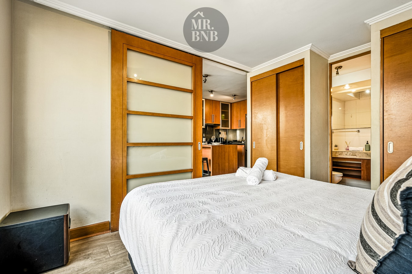Dormitorio con cama y puertas correderas hacia el pasillo y la cocina al fondo