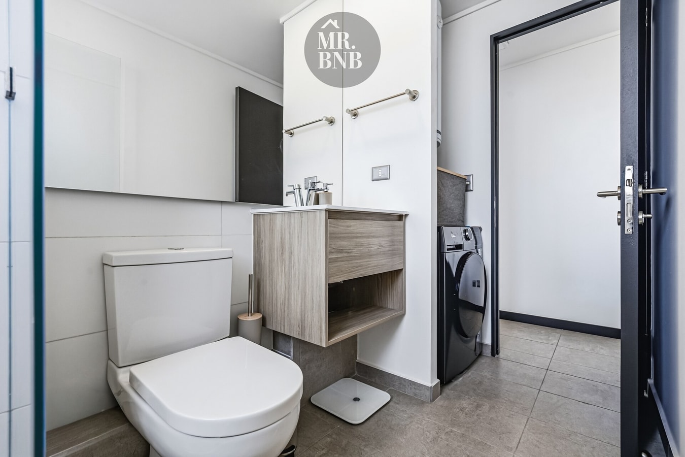 Baño con inodoro, mueble vanitorio y lavadora del departamento junto a la puerta