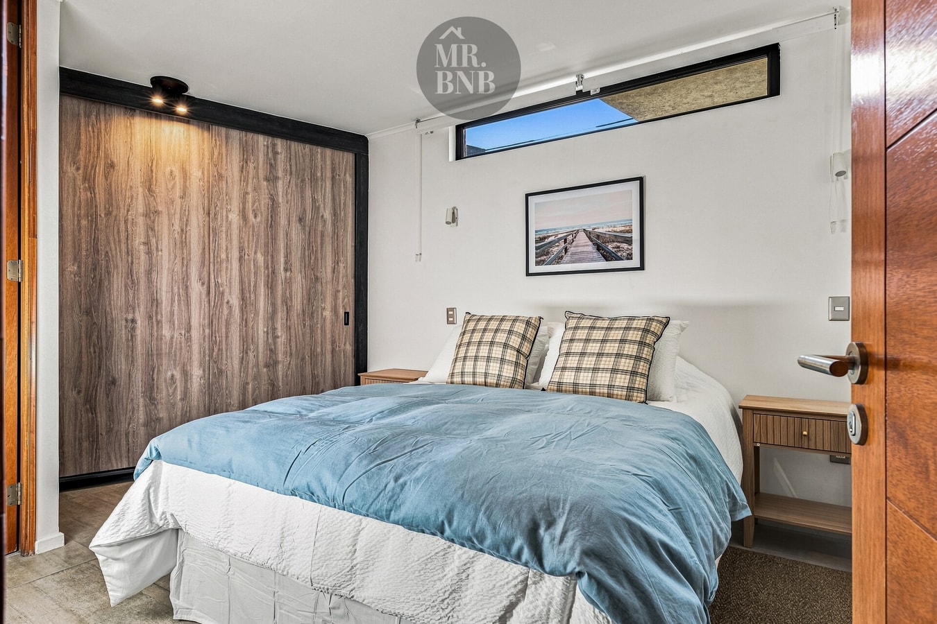 Dormitorio con cama, cubrecama celeste, veladores, closet de madera y cuadro