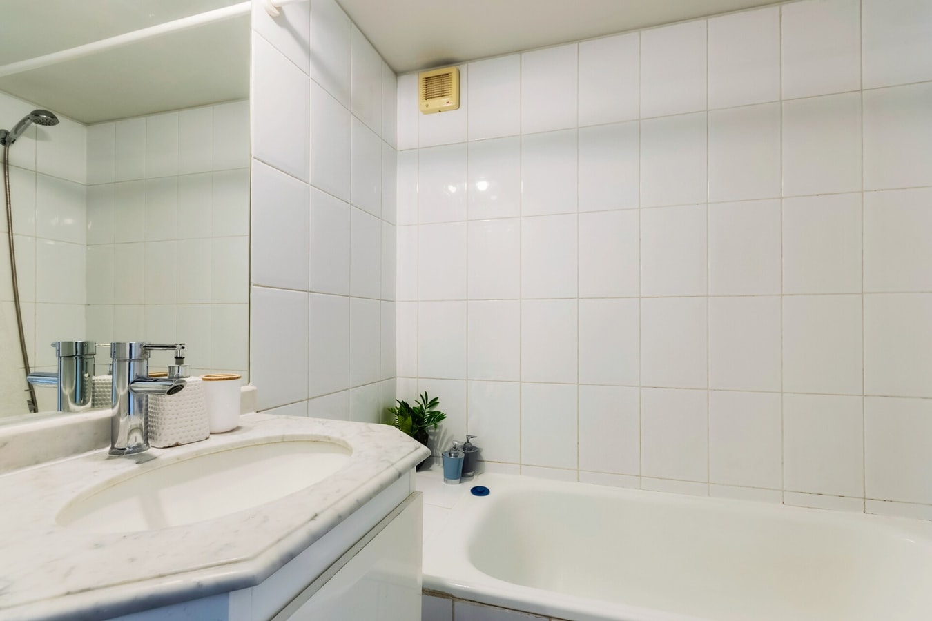 Baño con tina, revestimiento cerámico blanco y llave de ducha