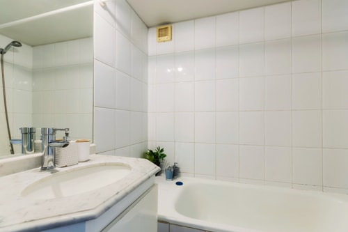 Baño con tina, revestimiento cerámico blanco y llave de ducha