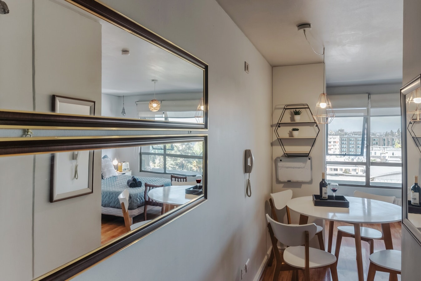 Estudio con espejo grande de piso, dormitorio reflejado y mesa con sillas junto a la ventana