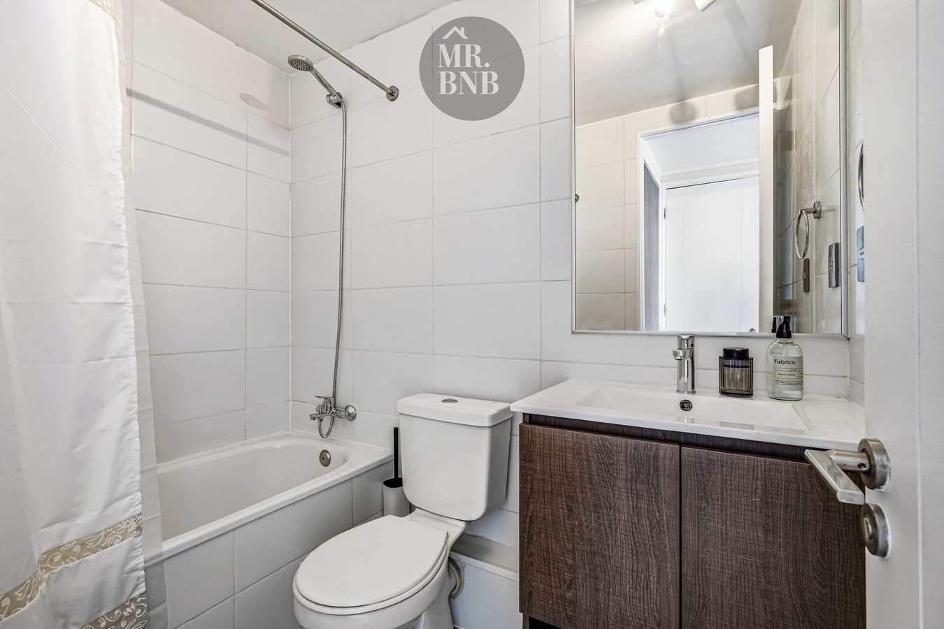 Baño con tina, cortina de ducha, mueble oscuro con lavamanos e inodoro