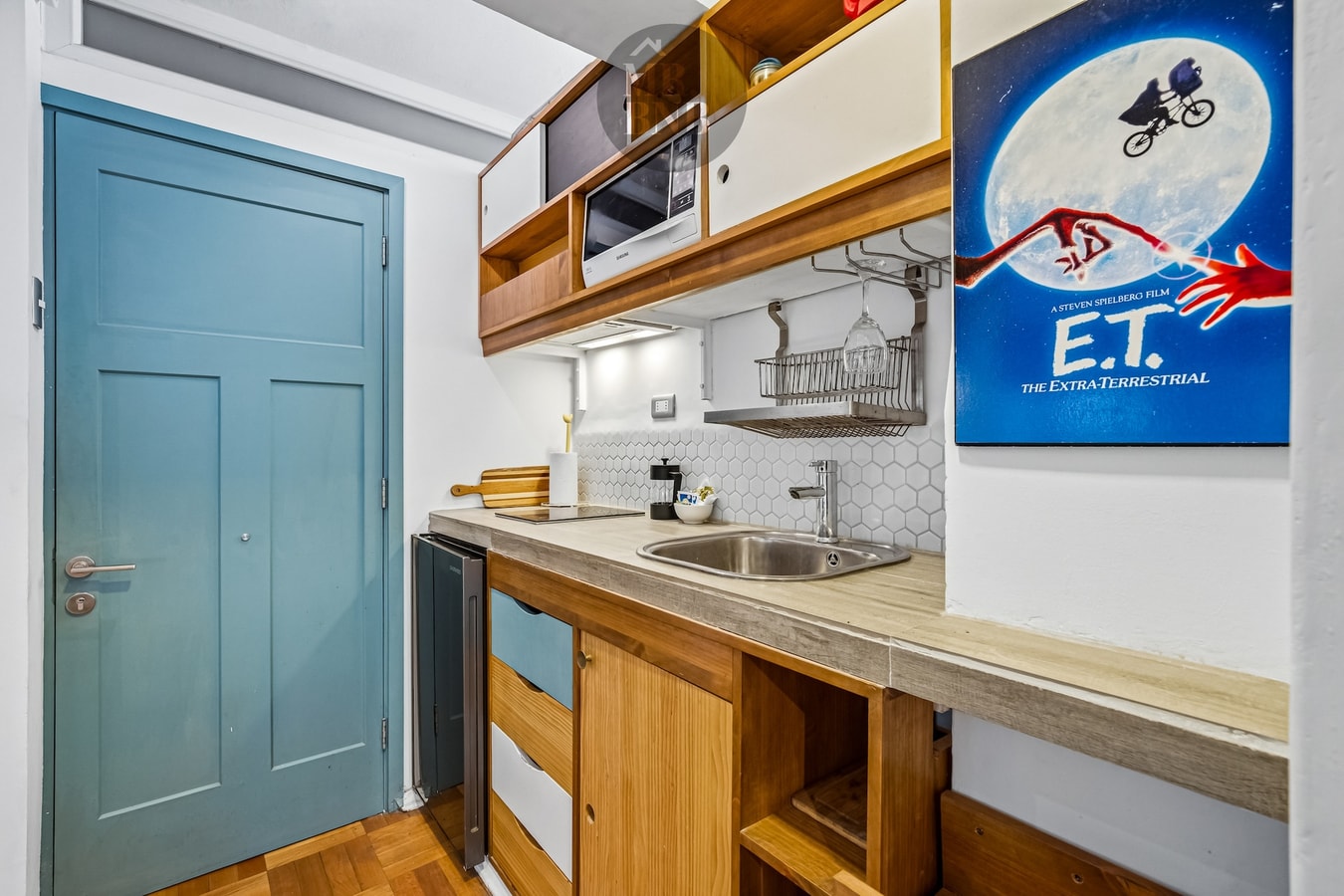 Kitchenette de suite con puerta azul, microondas y afiche decorativo