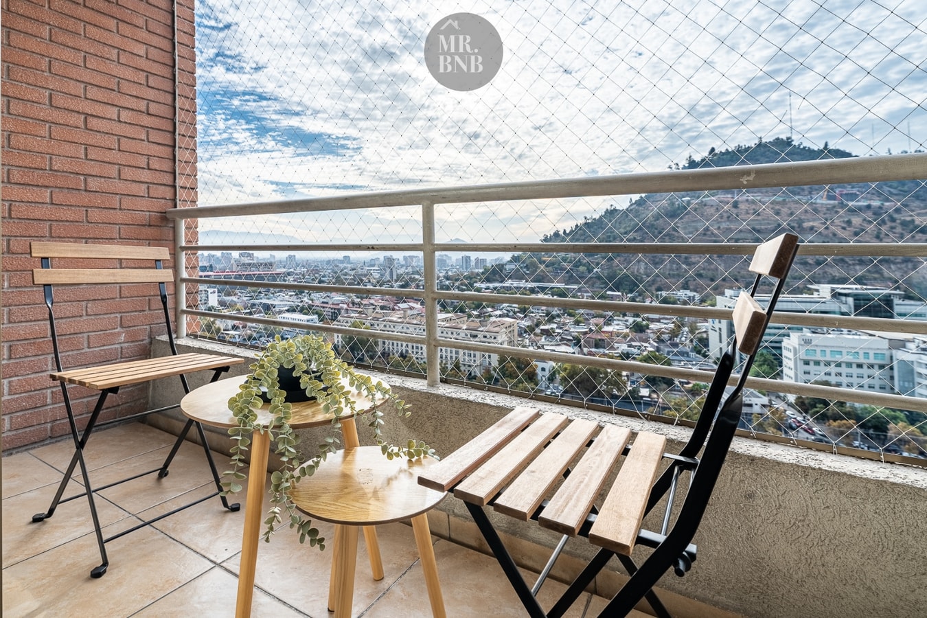Terraza con mesa y dos sillas plegables junto a la baranda, con vista al cerro San Cristóbal y la ciudad