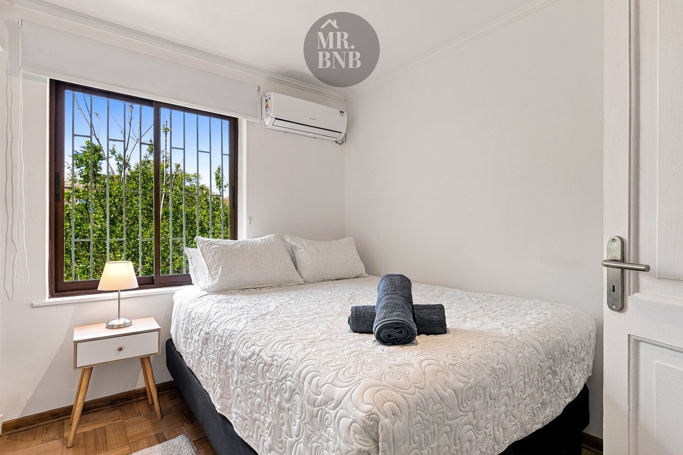 Dormitorio con cama matrimonial, aire acondicionado y ventana a los árboles.