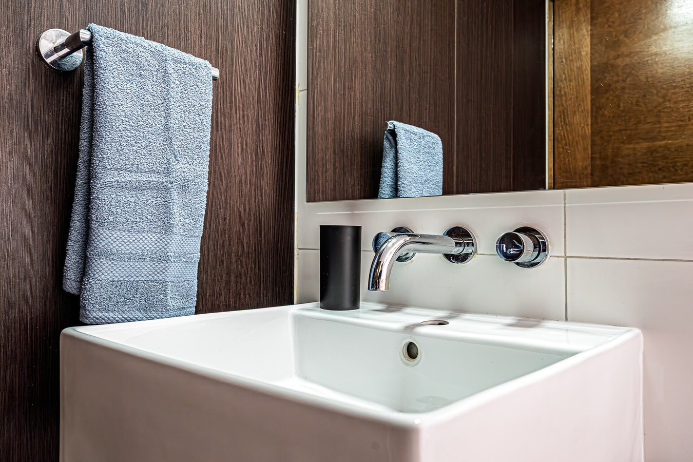 Detalle de lavamanos con grifería de pared y toallas