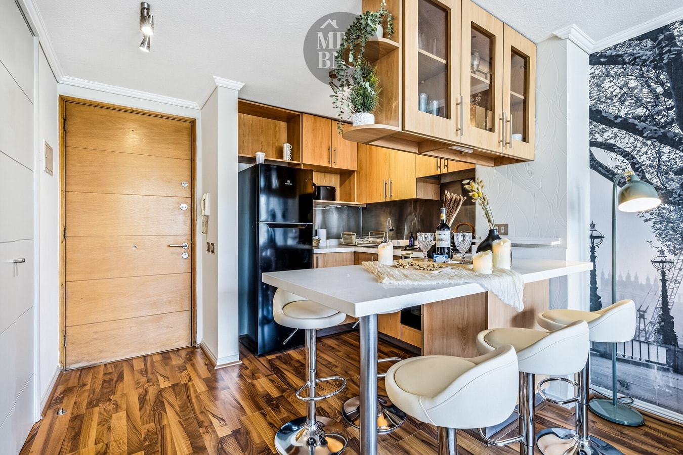 Hall de entrada con puerta de acceso, cocina y barra alta con sillas.